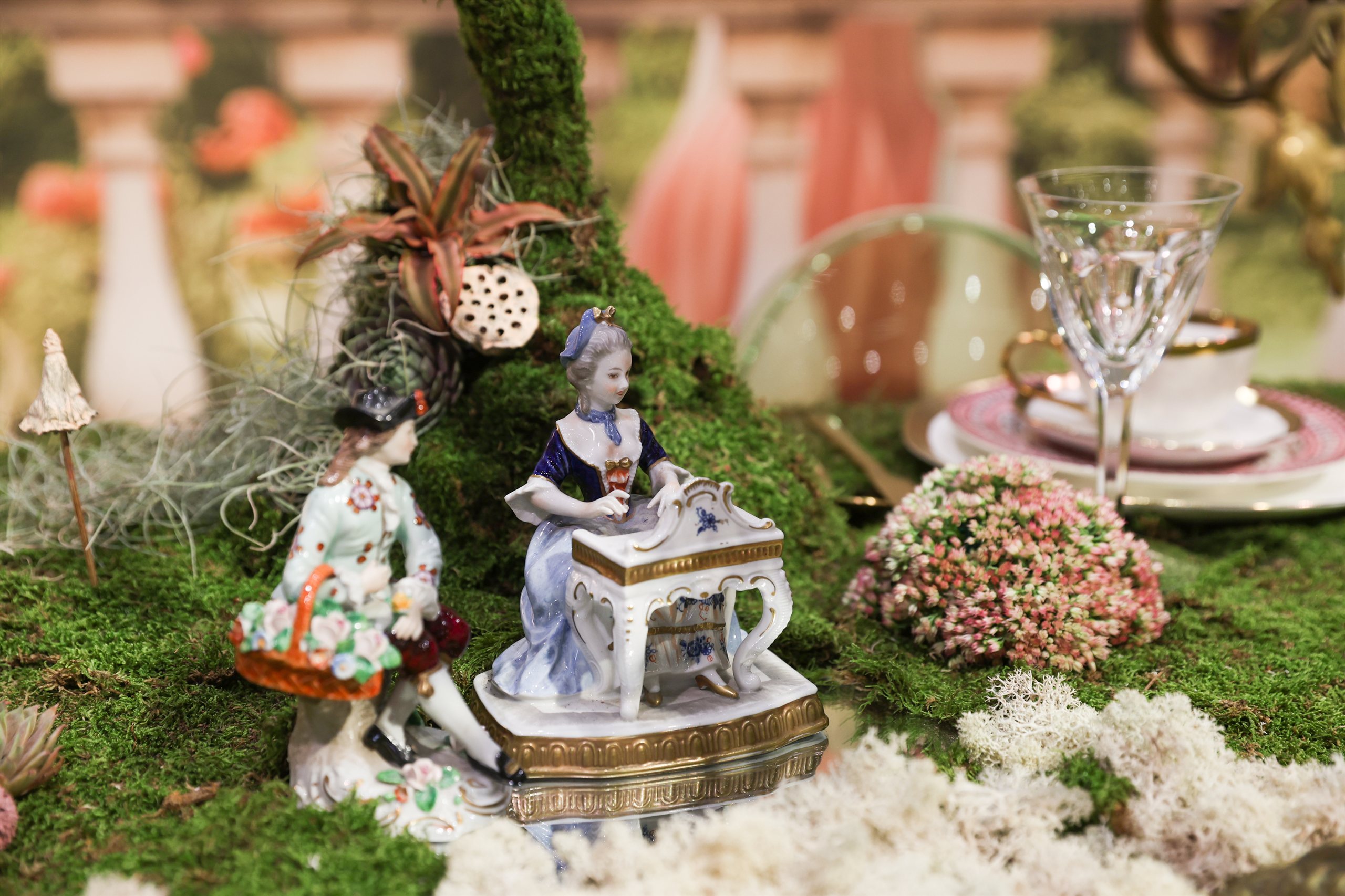 Antique porcelain figurines nestled among moss and dried flowers on the installation table
